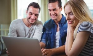 Smiling friends sitting at table and using laptop in cafÃ©