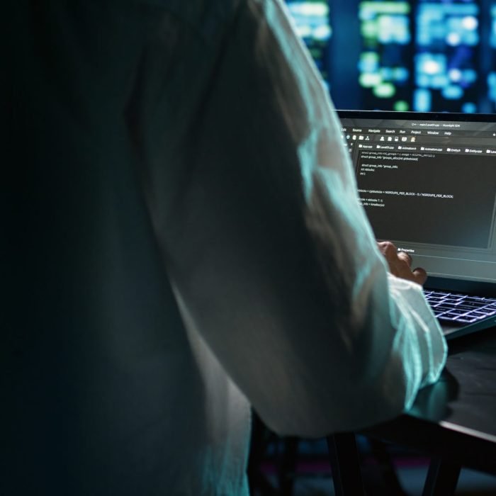 Licensed programmer running code on laptop, troubleshooting and updating data center equipment designed to accommodate server clusters, networking systems and storage arrays, close up